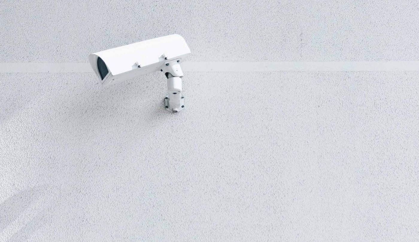 Close-up of a CCTV security camera mounted on an exterior wall, part of the community's 24-hour surveillance